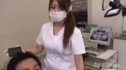 Japanische Zahnärztin mit Mundschutz und weißem Kittel blickt lüstern auf den Patienten hinab