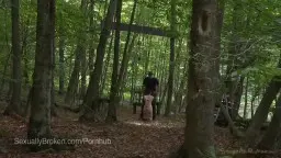 Nackte blonde Frau wird von einem Mann mit Seil durch sonnigen Wald geführt