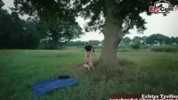 Blonde mit Pferdeschwanz und tätowierter Brünetter mit Mikrofon auf einer grünen Wiese vor einem Mann