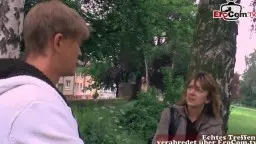 Junge Cosplay-Schlampe in grauer Jacke lehnt wartend an einem Baum im Park, während ein Mann im weißen Hoodie auf sie zugeht.