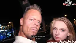 Nahaufnahme eines blonden Mannes mit Irokesenschnitt und einer lächelnden jungen Blondine, die sich nachts auf der Straße tief in die Augen schauen.