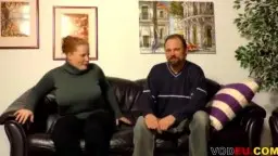 Molliges Paar sitzt entspannt nebeneinander auf schwarzer Ledercouch im Wohnzimmer