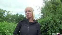 Lachende blonde MILF mit Hoodie steht vor dichtem grünem Gebüsch